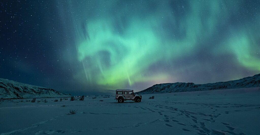 Offroad-Fahrzeug auf den Lofoten bei Nacht unter leuchtenden Polarlichtern am Himmel.