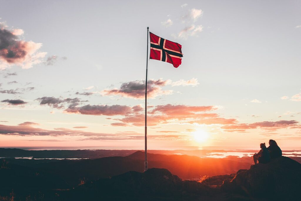 Norwegische Flagge weht im sanften Licht der Mitternachtssonne – symbolisch für die Einreise nach Norwegen
