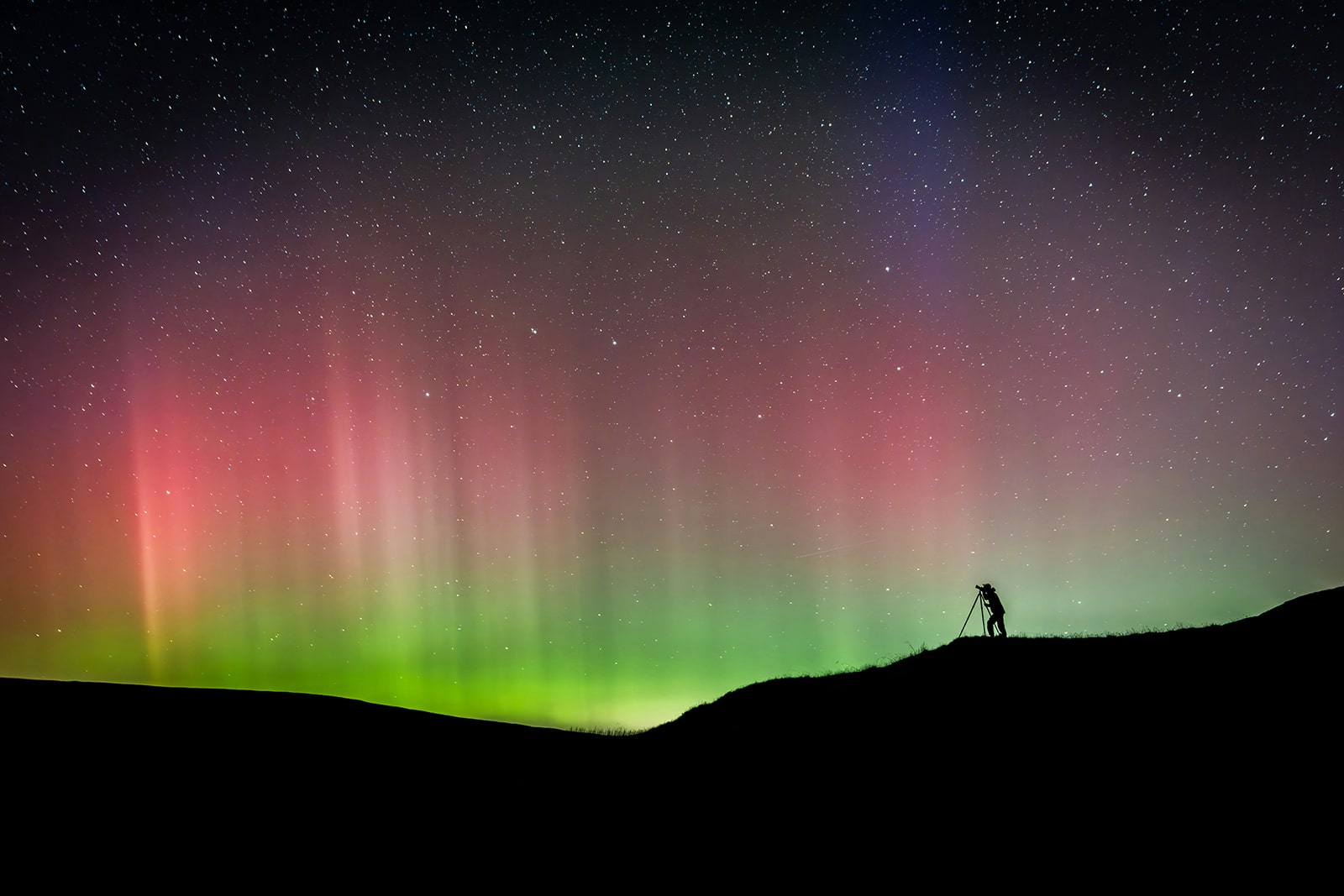 Fotograf mit Stativ beobachtet die Nordlichter am Himmel über Nordnorwegen.