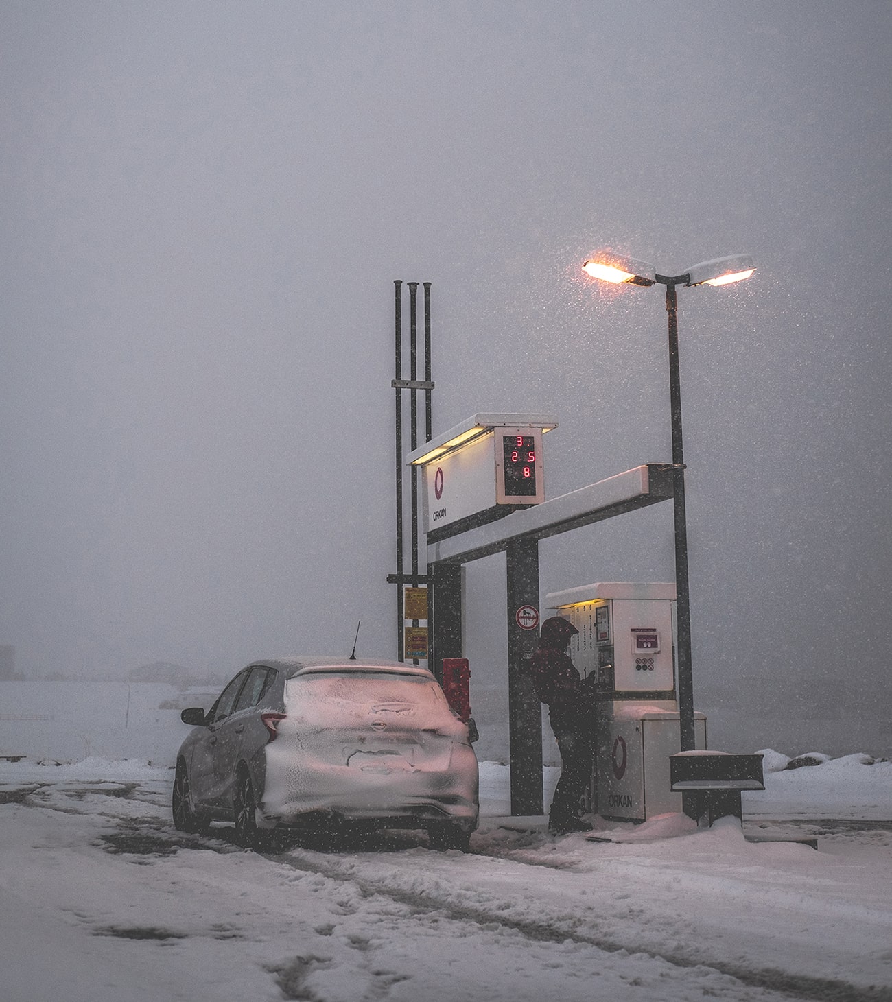 Verschneites Auto beim Tanken im Schneesturm, Winterfahrten Norden