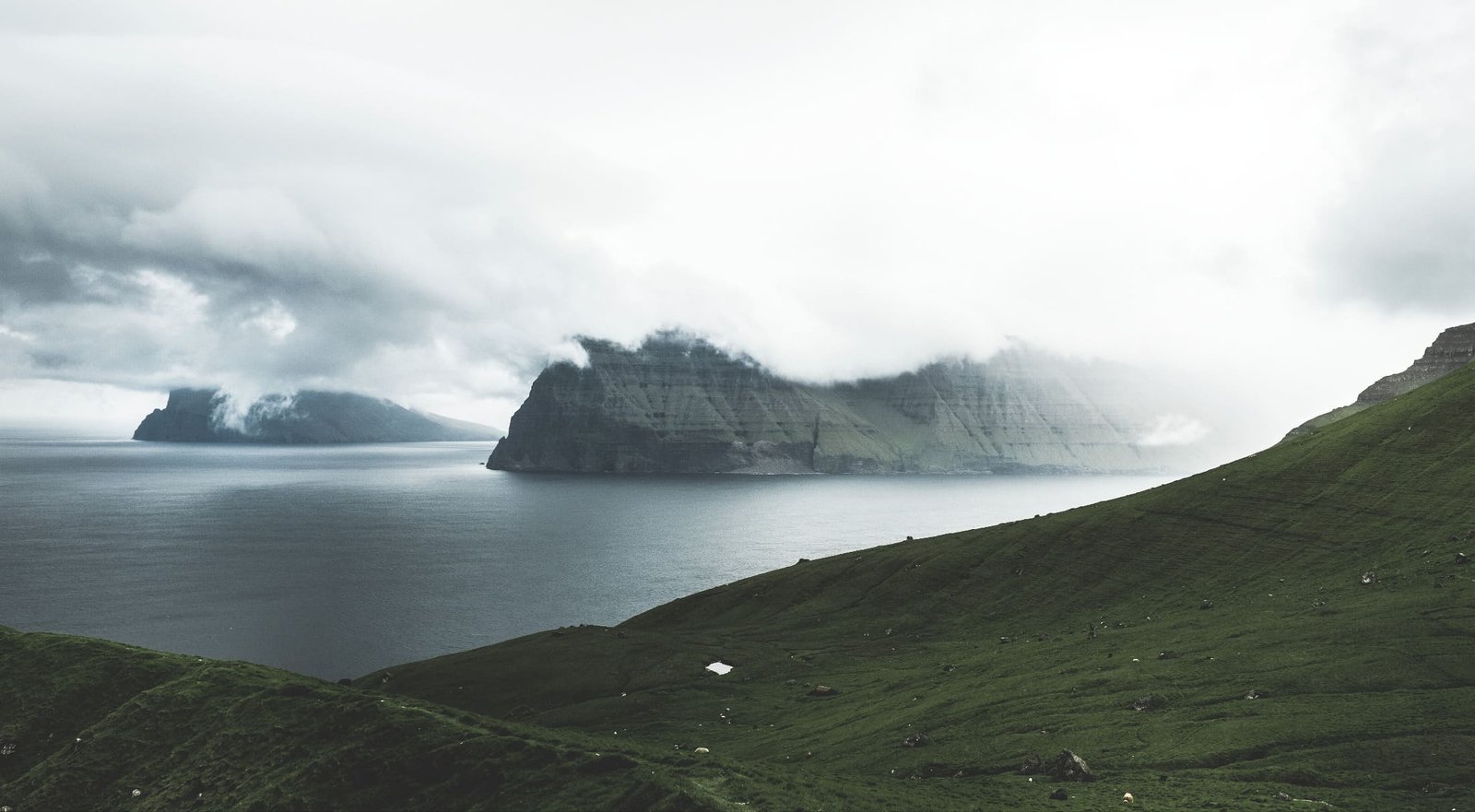 Wolken ziehen über die steilen Klippen von Kalsoy auf den Färöer Inseln, davor das Meer.