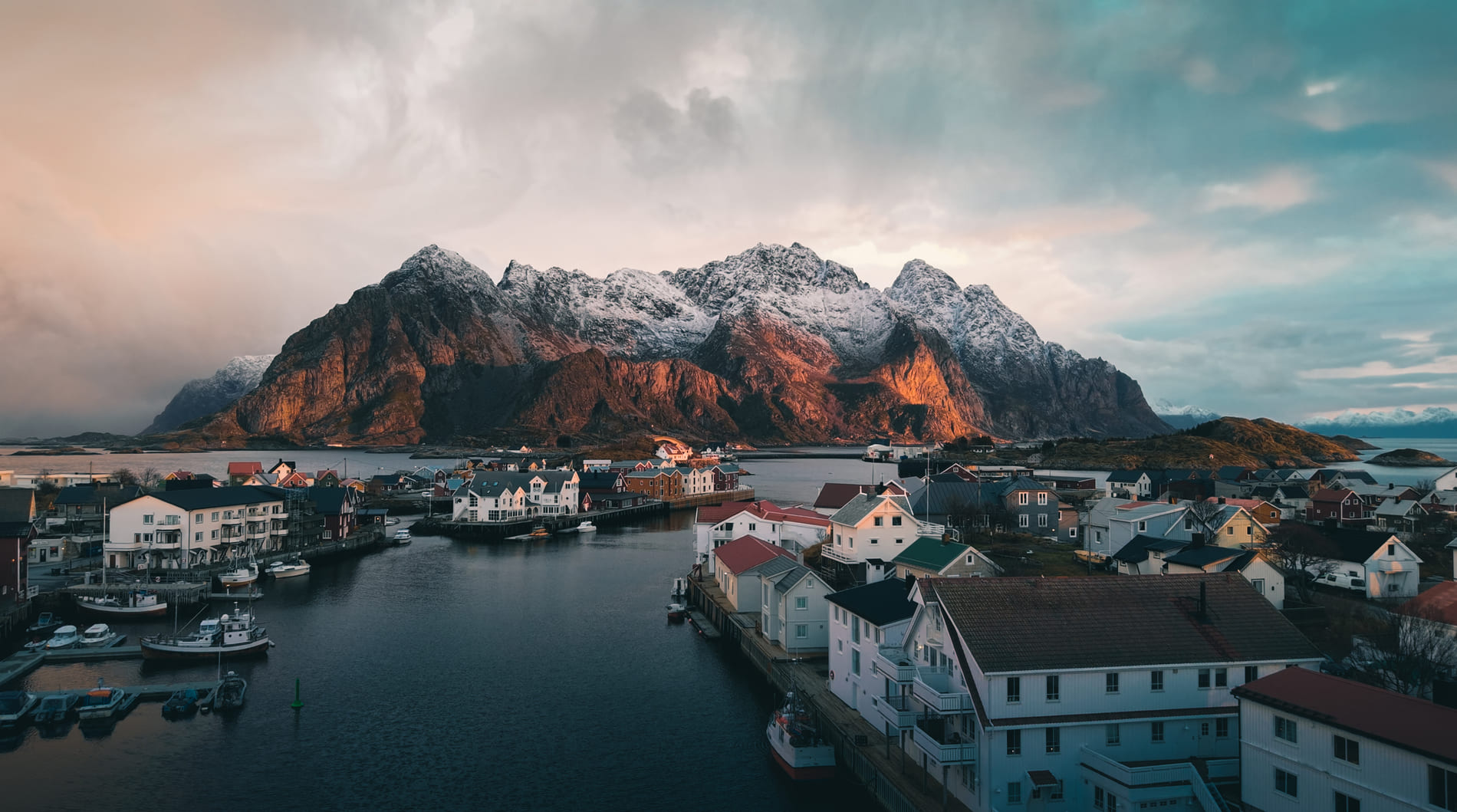 Henningsvær im goldenen Winterlicht auf den Lofoten, sonnenbeschienene Berge, Hafen und Rorbuer im Zentrum des Dorfes.