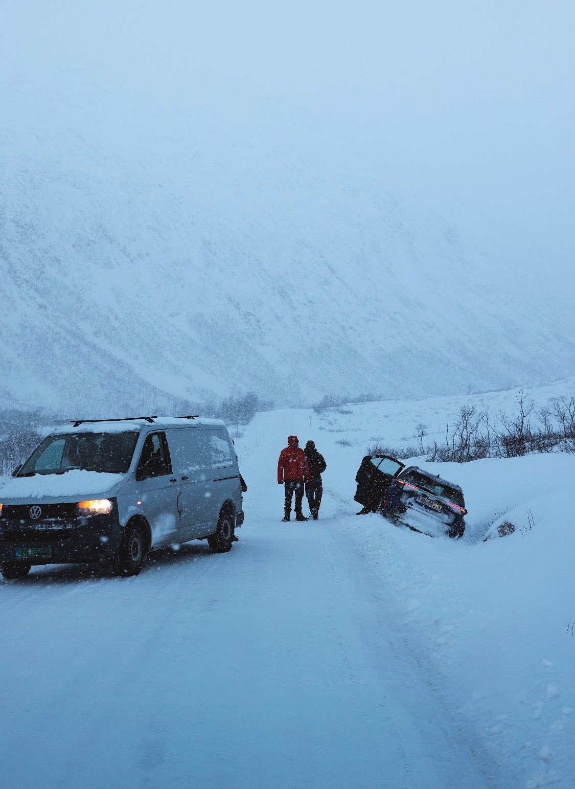 Verunfallter Mietwagen im Straßengraben bei Schneetreiben in Nordnorwegen, Rettungsfahrzeug daneben