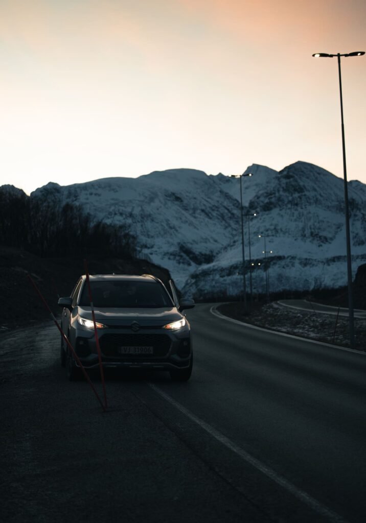 Suzuki Across 4×4 auf einer Straße in Nordnorwegen, verschneite Berge im Hintergrund bei rosa Morgendämmerung.