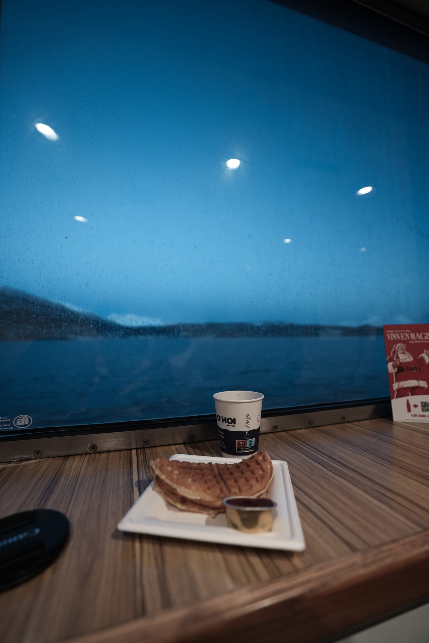 Waffel und Kaffeebecher am Fenster der Fähre über den Ullsfjord Richtung Svensby, draußen der Fjord in der blauen Stunde